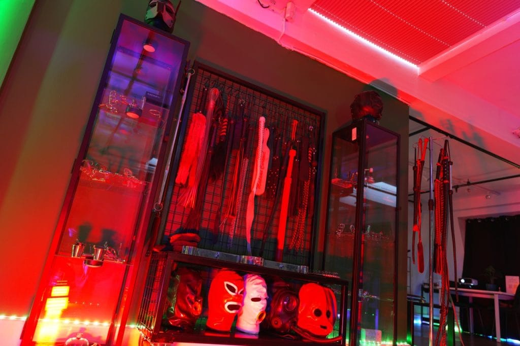 Display wall of paddles and restraints with red rubber hoods on mannequin heads