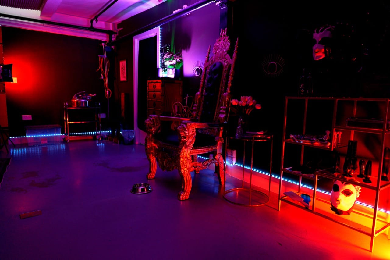Gilded throne and display shelving in the main chamber of London Dungeon Suite under purple and red light