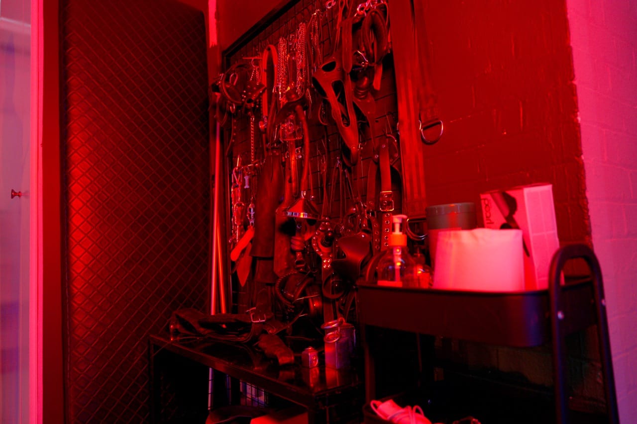 Wall rack of leather restraints and impact tools under red light