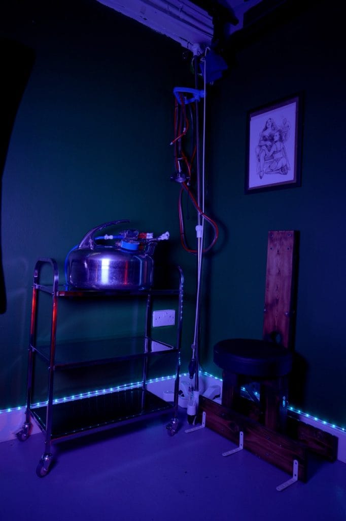 Medical corner with a stainless-steel trolley and drip stand against a dark teal wall