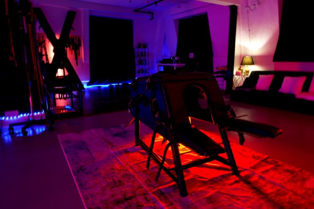 Main chamber of London Dungeon Suite with a St Andrew’s cross and padded bench under red and blue lighting