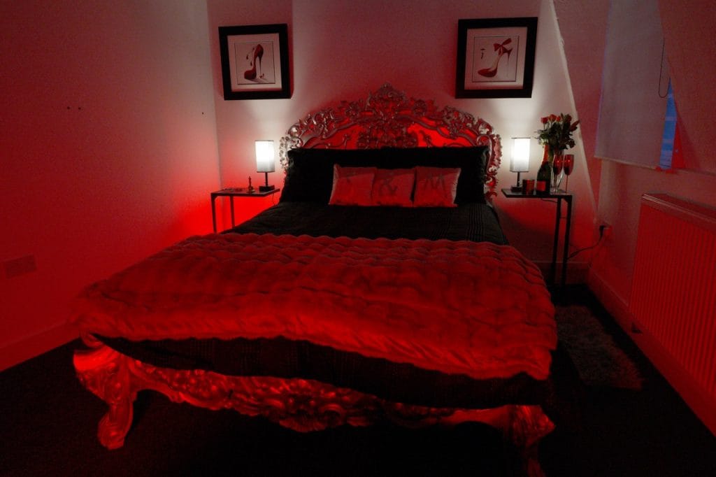 Bedroom of the London Dungeon Suite penthouse with an ornate double bed under red light