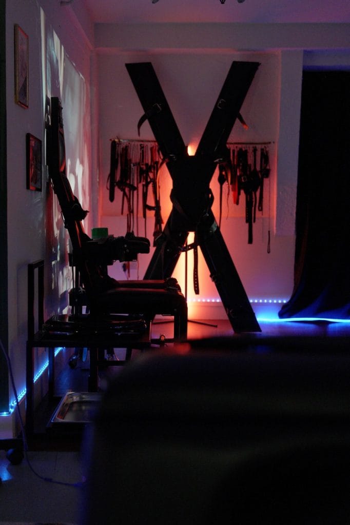 St Andrew’s cross and toilet chair seen across the room in low red and blue light